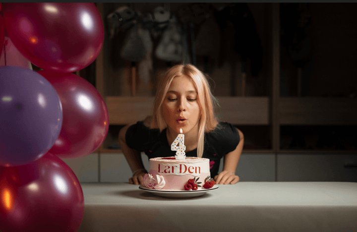 Lara spegne una candelina con il numero quattro su una torta di compleanno LarDen accanto a palloncini colorati