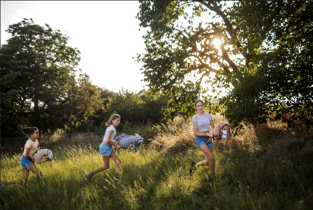 Children running with Hobby Horses through a sunny grassy field