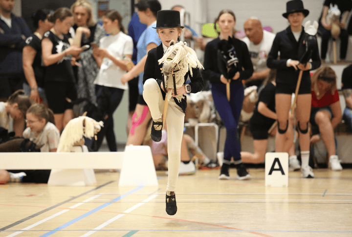 Young participant jumping with a white Hobby Horse at an indoor Hobby Horsing event