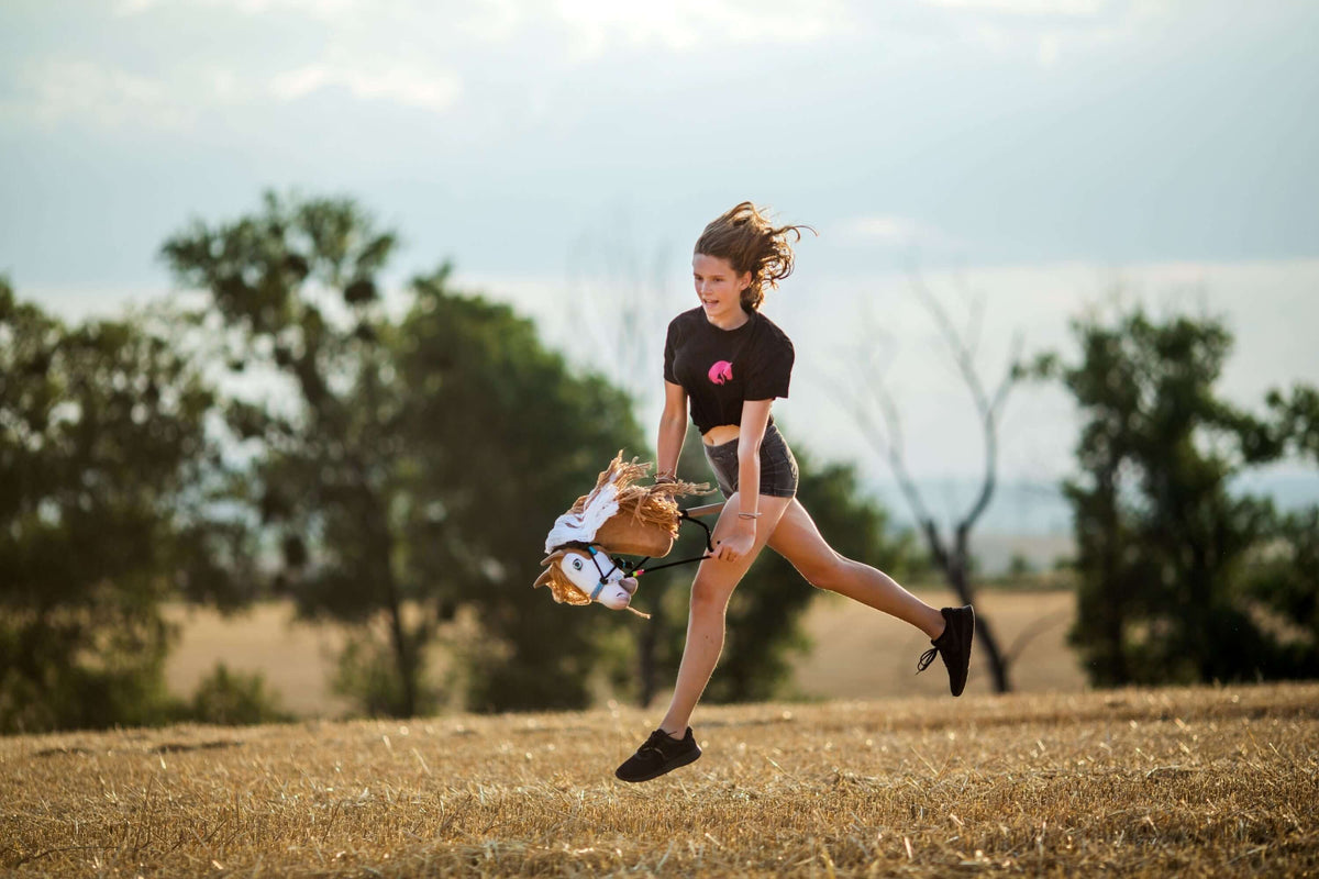 Young girl jumping outdoors with a Hobby Horse during Hobby Horsing training