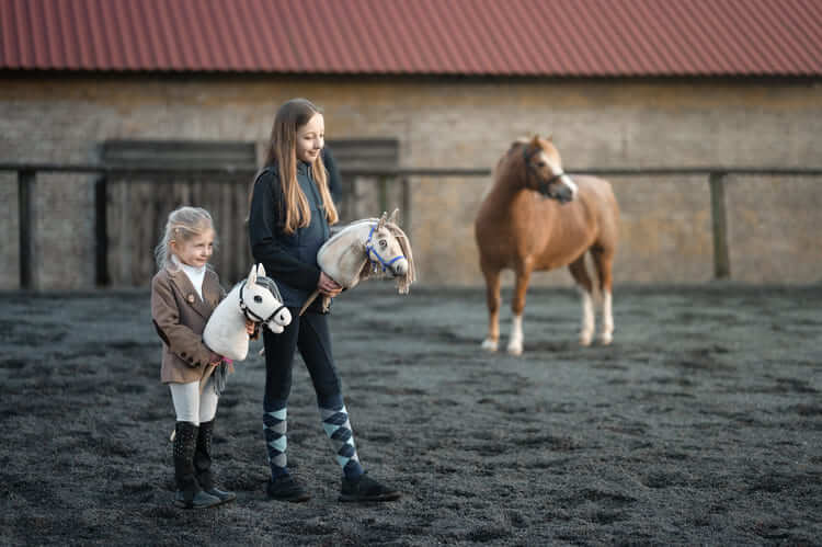 Due bambini trasportano Hobby Horses in un'arena all'aperto accanto a un pony
