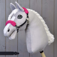 Cavezza nera con pelliccia rosa - similpelle di Hobby Horse LarDen con testa in peluche grigio chiaro, dettagli in pelliccia rosa, criniera bianca in filato e cavezza nera su bastone di legno, su sfondo di assi di legno.