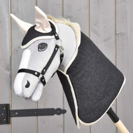 The Set Blue Denim by Hobby Horse LarDen features a handmade hobby horse with a blue denim head and wooden stick, creating a charming decoration that stands out against a light wood panel background.