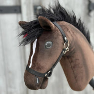 Primo piano di Hobby Horse Lucas con capezza nera di Hobby Horse LarDen, uno stallone hannoveriano marrone con criniera nera, lista bianca sul muso e capezza nera, su sfondo sfocato in legno.