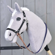 A plush hobby horse from Hobby Horse LarDen, featuring a light gray head, white mane, and face markings, wears Reins rubberized brown purple. It is positioned in front of a wooden wall.