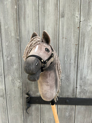 Hobby Horse Swing con cavezza nera - taglia S di Hobby Horse LarDen, con testa di cavallo in peluche su un bastone di legno, esposto davanti a una recinzione rustica grigia.