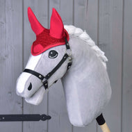 Hobby Horse grigio di Hobby Horse LarDen con criniera bianca, briglia nera e Cuffia all'uncinetto rossa per protezione dalle mosche, in piedi davanti a uno sfondo in legno chiaro.