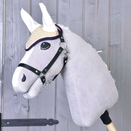 Hobby Horse LarDen in peluche grigio con cuffia all'uncinetto Nicol rossa, briglia e cappello di paglia, montato su un bastone di legno e mostrato davanti a uno sfondo di assi di legno.
