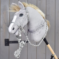 Set Start Argento (cavezza + redini a collare + lunghina + redini) di Hobby Horse LarDen su un Hobby Horse di peluche grigio con lista facciale bianca, montato su un bastone e appoggiato a una parete di legno grigia.