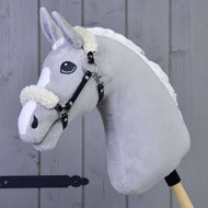 Cavezza nera con pelliccia - similpelle di Hobby Horse LarDen su un cavallo di peluche grigio con criniera bianca e cavezza nera, montato su un bastone di legno, davanti a uno sfondo con pannelli di legno.
