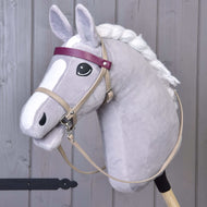 Hobby Horse LarDen con Hobby Horse grigio, criniera bianca, occhio nero e set Bordeaux in similpelle con briglia, redini e martingala, oltre a frontalino viola e muso in stile cartone animato. È in posizione verticale davanti a uno sfondo in legno.