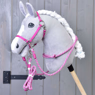 Set Start Rosa (cavezza + redini a collare + lunghina + redini) di Hobby Horse LarDen su Hobby Horse di peluche grigio con criniera bianca, montato su bastone in legno davanti a una parete in legno grigio.