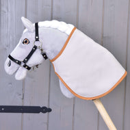 Hobby Horse LarDen grigio con criniera bianca, briglia nera e Coperta inglese marrone a quadri doppia faccia, montato su un bastone di legno davanti a una parete in legno grigia.