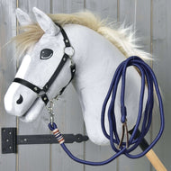 Corda per lavoro a terra Hobby Horse di Hobby Horse LarDen con cavallo grigio con criniera soffice, occhi in stile cartoon, briglia nera e corda blu fissata a un bastone in legno, su parete di legno grigia.