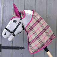 Hobby Horse LarDen Set Cubo Rosa con Hobby Horse imbottito dal muso grigio, briglia nera e coperta a quadri beige, rosa e neri, mostrato davanti a una parete di legno.