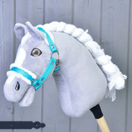 Hobby Horse grigio e bianco con criniera bianca intrecciata che indossa la Cavezza turchese con pelliccia Hobby Horse LarDen, l’accessorio perfetto, davanti a uno sfondo in legno grigio chiaro.