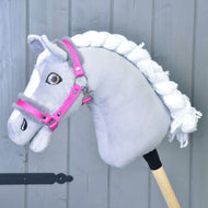 Hobby Horse LarDen "Cavezza rosa con pelliccia" mostrata su un Hobby Horse grigio con criniera bianca in filato, marcature facciali bianche e montato su un bastone di legno, su sfondo in legno grigio.