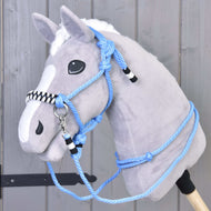 A plush hobby horse with gray fur, white mane, and blaze, features the Rope set Malibu—a blue rope halter with black and white accents plus matching reins—mounted on a wooden stick against a gray wooden background.