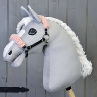 Hobby Horse in peluche Hobby Horse LarDen con muso grigio, criniera bianca e cavezza nera con pelliccia rosa antico in similpelle, mostrato su sfondo in legno.