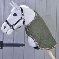 Un Hobby Horse di peluche grigio su bastone, con la Coperta Sport verde di Hobby Horse LarDen con bordatura arancione e cavezza nera, davanti a una parete in legno con cerniera in ferro nero.