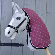 Hobby Horse grigio di Hobby Horse LarDen con briglia nera, cappuccio color bordeaux con motivo a stelle e Coperta da scuderia Viola, davanti a uno sfondo di legno grigio. Presenta lista bianca sul muso e occhi neri a bottone.