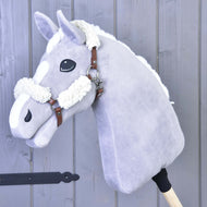 Cavezza marrone con pelliccia completa - similpelle Hobby Horse LarDen su Hobby Horse in peluche grigio chiaro con criniera e marcature bianche, montato su un bastone di legno e fotografato su sfondo di pannelli in legno grigio.