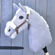 Hobby Horse in peluche grigio Hobby Horse LarDen con criniera bianca e cavezza marrone in similpelle con finitura in pelliccia, montato su un bastone di legno e mostrato davanti a una parete in legno grigio.