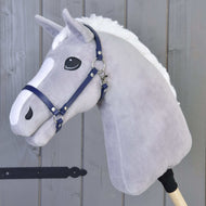 Hobby Horse in peluche grigio con criniera bianca e Cavezza - similpelle blu scuro di Hobby Horse LarDen, su un bastone di legno davanti a una parete di legno grigio.