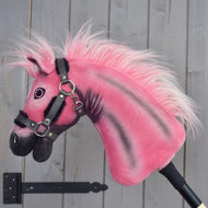 Hobby Horse LarDen Pinkie con cavezza glitterata di Hobby Horse LarDen, edizione limitata, montato su un bastone e posizionato davanti a una parete di legno grigia.