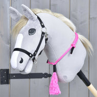 The Hobby Horse LarDen "Cordeo Pink Festive" is a plush gray hobby horse with a white mane, black bridle, handmade cordeo, pink rope harness, and pink tassel, pictured against a wooden background.