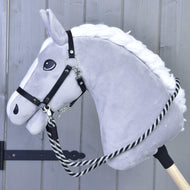 The Hobby Horse LarDen “Hobby Horse – Reins black stripe” is a plush gray hobby horse with a white mane and black bridle, handmade with striped black-and-white polypropylene reins on a wooden stick against a light gray wooden background.