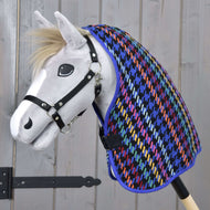 Hobby Horse giocattolo bianco con cavezza nera che indossa la colorata Coperta da scuderia Peru di Hobby Horse LarDen con motivo pied-de-poule, su sfondo di legno chiaro.