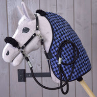 Un Hobby Horse in peluche Set Harmony Blu di Hobby Horse LarDen con cavezza nera, redini e coperta da scuderia pied-de-poule blu e nera è montato a parete su sfondo di assi di legno chiaro.