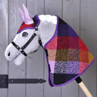 The Hobby Horse LarDen Set Autumn Plaid 2 features a plush gray-faced hobby horse with a black bridle and a colorful patchwork plaid neck, mounted on a wooden stick, shown against a wooden wall.