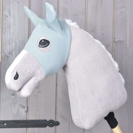 Hobby Horse LarDen "Maschera Hobby Horse Spiky" con cavallo grigio in peluche, briglia azzurra, criniera bianca e maschera protettiva su bastone di legno, mostrato davanti a uno sfondo di assi di legno chiaro.