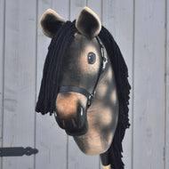 Hobby Horse LarDen’s Hobby Horse Stormy with Black Halter, a realistic dapple grey Hanoverian stallion with a black yarn mane and brown plush head mounted on a stick, is shown in front of a light gray wooden wall.