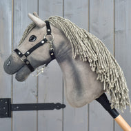 Hobby Horse Swing con Cavezza nera, taglia S, di Hobby Horse LarDen, ispirato all'eleganza di uno stallone hannoveriano e con criniera in filato grigia, briglia nera e occhi a bottone, montato su un bastone di legno e fotografato su uno sfondo in legno grigio.