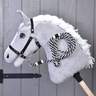The Hobby Horse LarDen "Hobby Horse - Lead rope stripe black" features a plush horse with white mane, black bridle, and a black-and-white striped lead rope on a wooden stick, displayed against a wooden wall.
