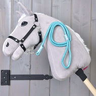 The Hobby Horse LarDen "Hobby Horse - rope stripe Atlantis" features a gray plush head with a black bridle and blue rope leash, mounted on a wooden stick and displayed against vertical wooden planks.