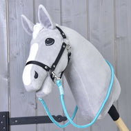 Hobby Horse LarDen Reins Atlantis, un Hobby Horse in peluche grigio con briglia nera e redini blu in corda di polipropilene su un bastone di legno, mostrato davanti a una parete rustica in legno.
