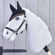Hobby Horse grigio di Hobby Horse LarDen con redini nere e criniera bianca che indossa la Cuffia all’uncinetto Black Gold per la protezione dagli insetti, con dettagli neri sul muso, su sfondo in legno chiaro.