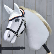 Hobby Horse LarDen Cuffia Speedy con Hobby Horse grigio realistico, briglia nera, criniera bianca e cuffia per orecchie bianca protettiva contro le mosche, montato su un bastone di legno davanti a una parete in legno grigio chiaro.