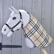 Hobby Horse LarDen "Coperta Cremo England": un Hobby Horse grigio con cavezza nera e coperta beige a quadri, con cuffietta antimosche per protezione dagli insetti, montato su un bastone di legno davanti a una parete in legno grigio.