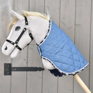 Hobby Horse di peluche su bastone di legno con Hobby Horse LarDen Coperta Beautiful Jeans e cavezza nera, posizionato davanti a una parete in legno chiaro per una protezione aggiuntiva.