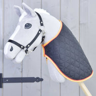 Coperta Flag di Hobby Horse LarDen, un giocattolo Hobby Horse grigio con briglia nera e coperta trapuntata con bordatura arancione, montato su un bastone di legno davanti a una staccionata di legno grigia.