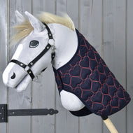 Hobby Horse in peluche con cavezza nera e coperta trapuntata per Hobby Horse “Blanket Pink Heart” di Hobby Horse LarDen, decorata con cuori rosa, posato su sfondo in legno.