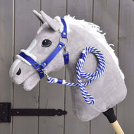 Hobby Horse LarDen Set Essential Blu con Hobby Horse grigio in peluche, criniera bianca, cavezza blu con bordo in pelliccia e redine in corda blu e bianca su un bastone di legno, mostrato davanti a una staccionata di legno grigia.