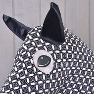 Primo piano della Tuta protettiva per Hobby Horse DeLuxe (Lycra) di Hobby Horse LarDen con tessuto in lycra lavabile geometrico bianco e nero, grandi orecchie nere e occhio cucito su sfondo in legno chiaro.