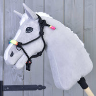 Cavezza in corda Arcobaleno di Hobby Horse LarDen su un Hobby Horse grigio con criniera bianca, perline color arcobaleno e cavezza in corda nera, montato su un bastone di legno e mostrato davanti a una parete di legno grigio chiaro.