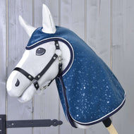 Hobby Horse LarDen "Raincoat Derby", un Hobby Horse in morbido peluche bianco con cavezza nera e impermeabile blu lucido decorato con gocce d’acqua, esposto su sfondo di assi di legno chiaro.
